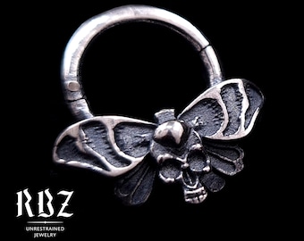 May include: A circular sterling silver hinged hoop ring featuring a detailed moth design with a skull at its center. The metal has an oxidized finish with dark recessed areas and polished highlights. Text reads RBZ UNRESTRAINED JEWELRY and Solid Sterling silver.