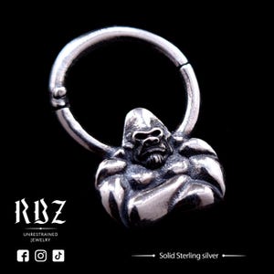 May include: A silver gorilla charm with arms crossed, attached to a silver hoop. The charm is detailed with a textured surface and a fierce expression.  Solid Sterling silver.