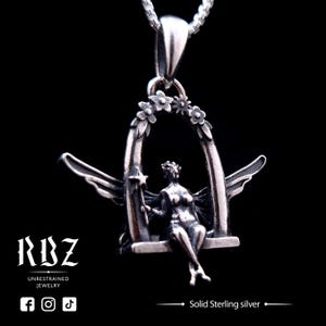 Puede incluir: Un colgante de plata con un hada sentada en un columpio, rodeada de flores. El colgante está hecho de plata de ley maciza y cuelga de una cadena de plata.