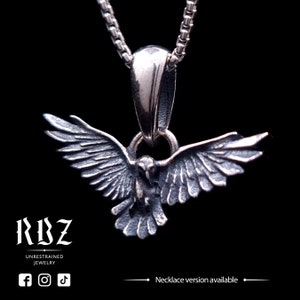 May include: A silver-toned metal pendant shaped like a bird with wings spread wide, suspended from a matching box chain. The pendant features detailed feather textures and a dark, oxidized finish. Text on the image reads RBZ UNRESTRAINED JEWELRY.
