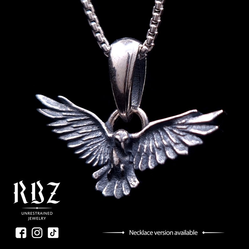 May include: A silver-toned metal pendant shaped like a bird with wings spread wide, suspended from a matching box chain. The pendant features detailed feather textures and a dark, oxidized finish. Text on the image reads RBZ UNRESTRAINED JEWELRY.