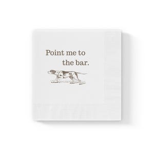 May include: White square paper napkins with a brown illustration of a dog and the text "Point me to the bar." The napkins have a ribbed border and are stacked.