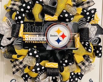 Könnte beinhalten: Ein dekorativer Kranz mit schwarzen, weißen und gelben Bändern in verschiedenen Mustern, darunter Punkte und Vichy-Karo. Der Kranz hat ein Nummernschild der Pittsburgh Steelers in der Mitte mit dem Teamlogo und -namen. Der Kranz wird an einer weißen Tür ausgestellt.