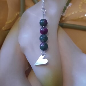 May include: A silver chain necklace with a silver heart charm and green and pink gemstone beads.