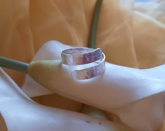 May include: A silver ring with a hammered texture, wrapped around a white flower.