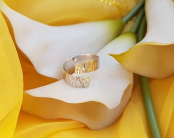 May include: A silver ring with a textured, hammered finish. The ring is open and has a curved design.