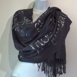 May include: A dark gray scarf with silver lettering that reads "Embrace the Wonder". The scarf has a fringe border.