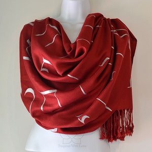 May include: A red pashmina shawl with a white abstract design. The shawl has a fringe border.