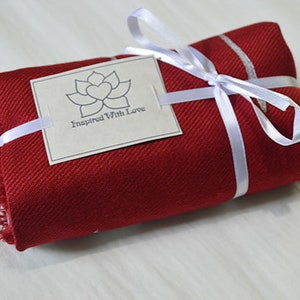 May include: A red scarf with white stripes is wrapped and tied with a white ribbon. A white tag with a gray lotus flower and the text "Inspired With Love" is attached to the ribbon.