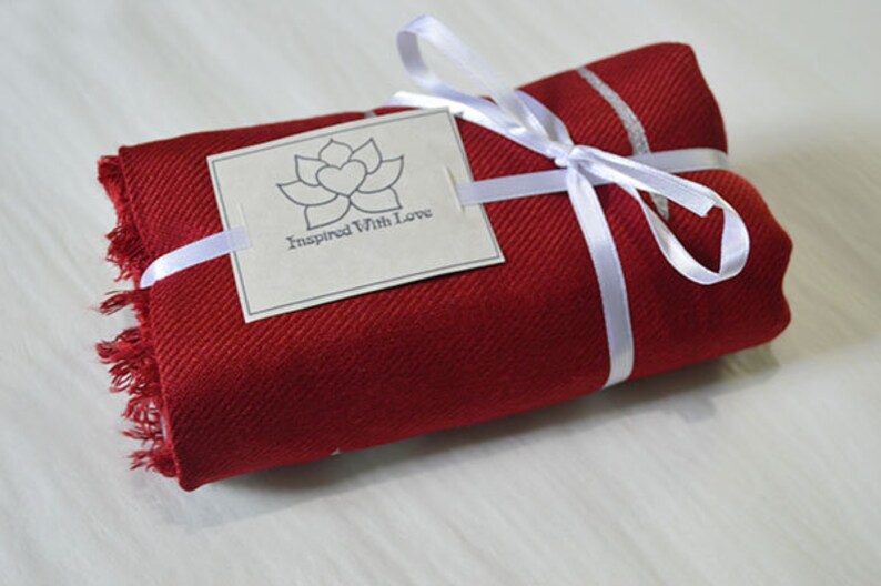 May include: A red scarf with white stripes is wrapped and tied with a white ribbon. A white tag with a gray lotus flower and the text "Inspired With Love" is attached to the ribbon.