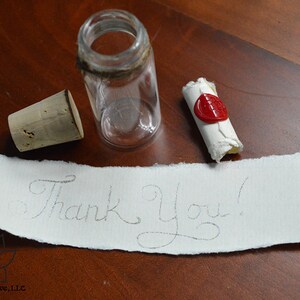 May include: A small glass bottle with a cork stopper and a rolled up piece of paper with a red wax seal. The paper has the words "Thank You!" written on it.