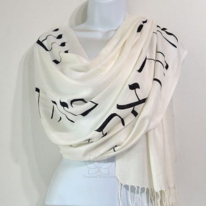 May include: White scarf with black Hebrew lettering. The scarf is made of a soft, lightweight fabric and has a fringed edge.