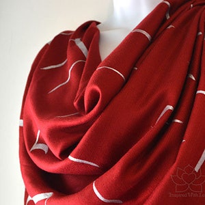 May include: A red scarf with a white abstract design. The scarf is made of a soft, lightweight fabric and is perfect for adding a touch of style to any outfit.