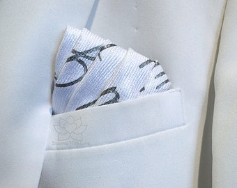 May include: A white pocket square with a black and silver design. The pocket square is folded and placed in the pocket of a white blazer.