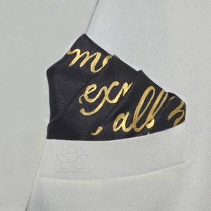 May include: A black pocket square with gold lettering that reads "more, explore, all the way".
