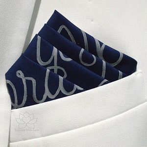May include: A navy blue pocket square with a white pattern of the word "aura" repeated across the fabric.