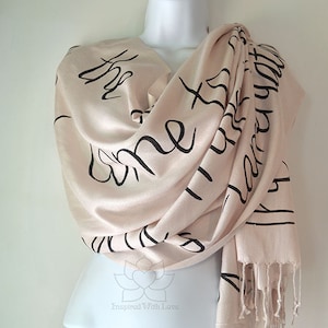 May include: A blush pink scarf with black calligraphy that reads "The best is yet to come".