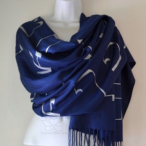 May include: A navy blue scarf with a silver pattern and fringe. The scarf is draped over a white mannequin. The silver pattern appears to be an abstract design. The scarf is made of a soft material.