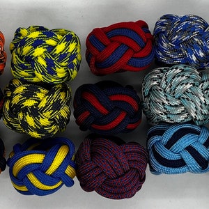 May include: A collection of 20 colorful, braided rope cufflinks. The cufflinks are made of various colors and patterns, including red, blue, green, yellow, and black.