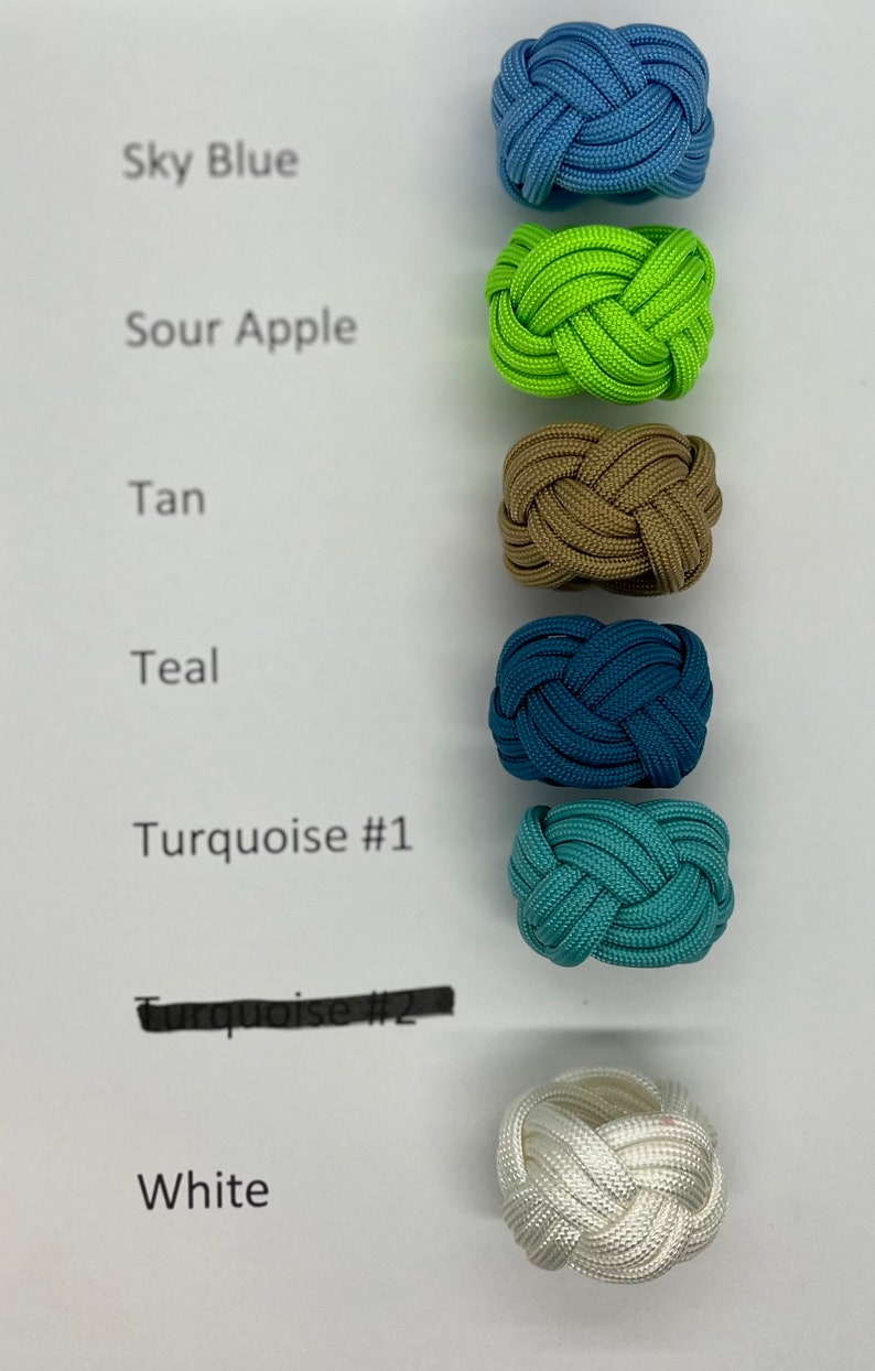 Puede incluir: Un conjunto de siete pulseras de paracord en varios colores, incluyendo azul cielo, verde manzana agria, marr&oacute;n, azul verdoso, turquesa y blanco. Las pulseras est&aacute;n dispuestas verticalmente sobre un fondo blanco con los nombres de los colores escritos junto a cada pulsera.
