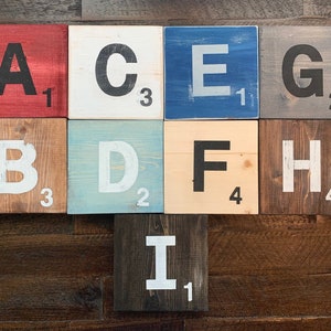 May include: Nine wooden tiles with letters A through I painted in white and black on different colored backgrounds. Each tile has a number on the bottom right corner.