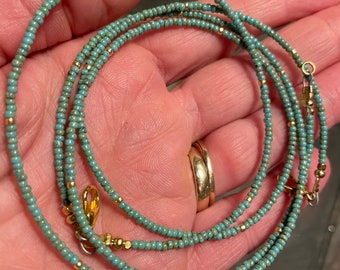 May include: Delicate turquoise beaded necklace with gold-colored accents and a clasp. The necklace is made of small, round beads strung together, creating a layered effect. The gold accents add a touch of elegance to the jewelry.