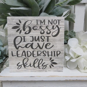 May include: A white wooden sign with a gray distressed finish. The sign reads "I'm not bossy I just have leadership skills".
