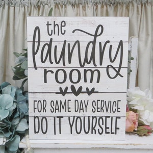 May include: White wooden sign with black text that reads "The Laundry Room &" with three hearts and "For Same Day Service Do It Yourself".