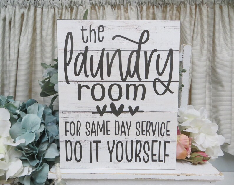 May include: White wooden sign with black text that reads "The Laundry Room &" with three hearts and "For Same Day Service Do It Yourself".
