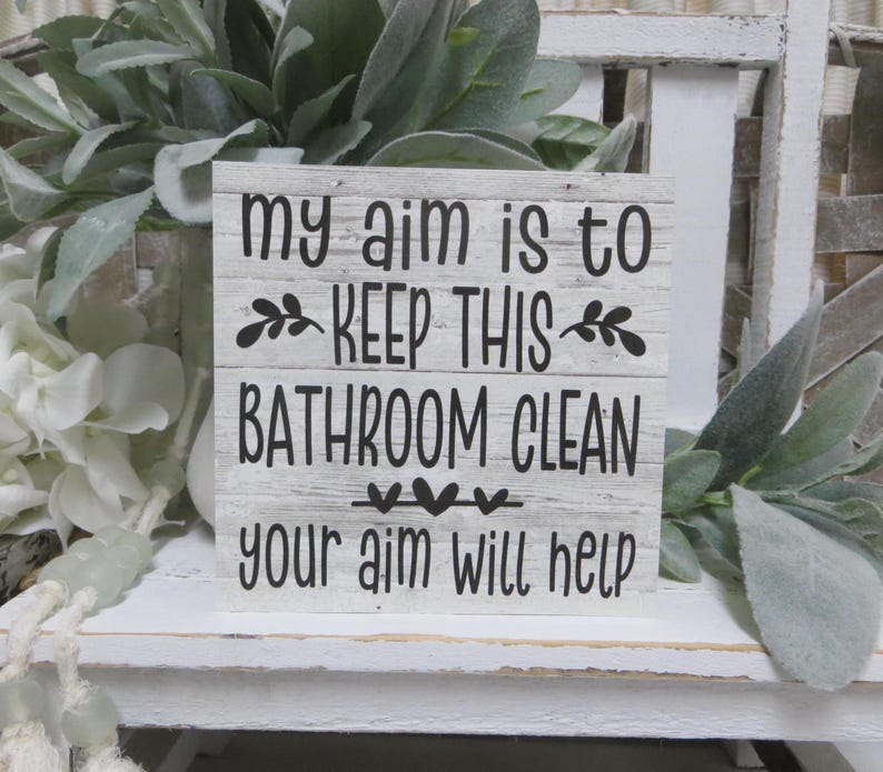May include: White wooden sign with black text that reads "My aim is to keep this bathroom clean. Your aim will help."