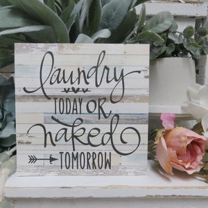 May include: A rustic wooden sign with a whitewashed background and a black handwritten message that reads "Laundry Today or Naked Tomorrow".