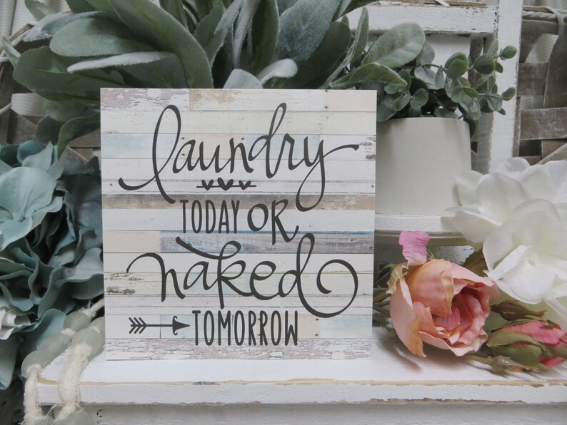 May include: A rustic wooden sign with a whitewashed background and a black handwritten message that reads "Laundry Today or Naked Tomorrow".