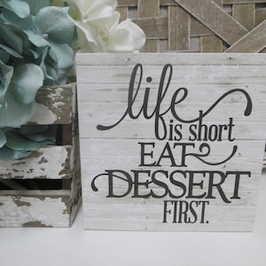 May include: White wooden sign with black text that reads "life is short eat dessert first".