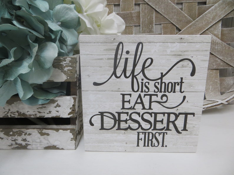 May include: White wooden sign with black text that reads "life is short eat dessert first".