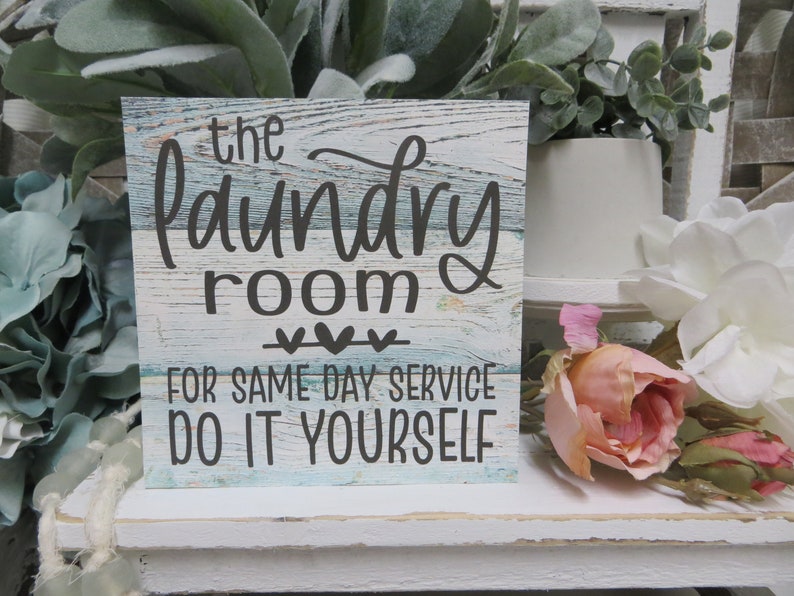 May include: A wooden sign with a blue and white distressed paint finish. The sign reads "The Laundry Room For Same Day Service Do It Yourself" with three small hearts above the text.