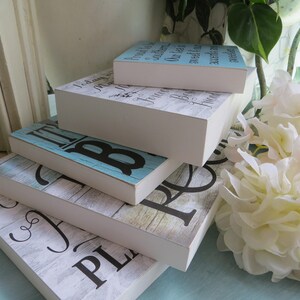 Peut inclure: Une pile de quatre pancartes en bois avec un fond blanc et des lettres bleues et noires. La pancarte du haut indique "Trouvez une raison de sourire chaque jour". La deuxi&egrave;me pancarte indique "Aujourd'hui est un bon jour pour &ecirc;tre heureux". La troisi&egrave;me pancarte indique "La vie est meilleure &agrave; la plage". La pancarte du bas indique "Bons moments et bons amis".