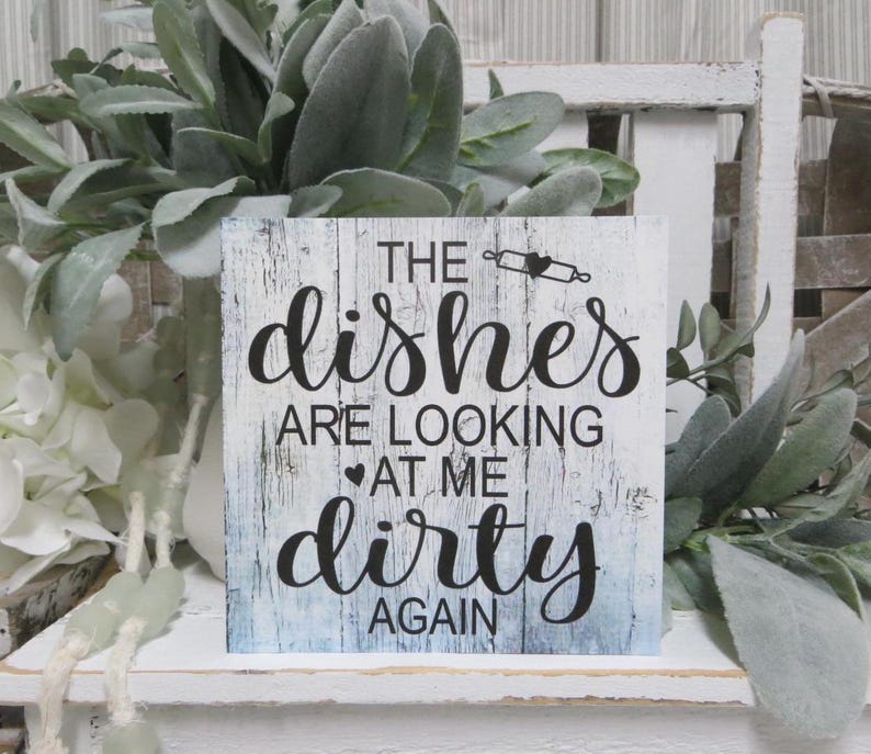 May include: White wooden sign with blue and white distressed paint. The sign says "The dishes are looking at me dirty again".