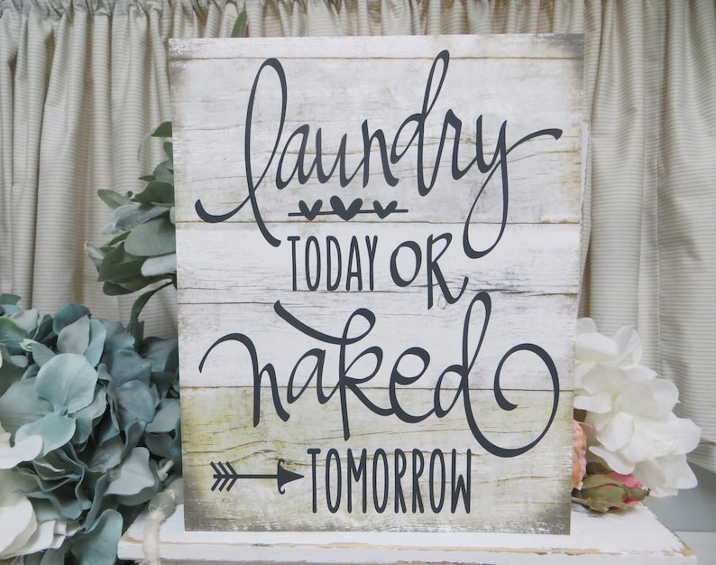 May include: White wooden sign with black lettering that reads "Laundry Today or Naked Tomorrow". The sign has a distressed wood look and a small arrow pointing to the right.