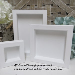 May include: Three white square picture frames of different sizes. The frames are made of wood and have a simple, modern design. All sizes will hang flush to the wall using a small nail and the cradle on the back.