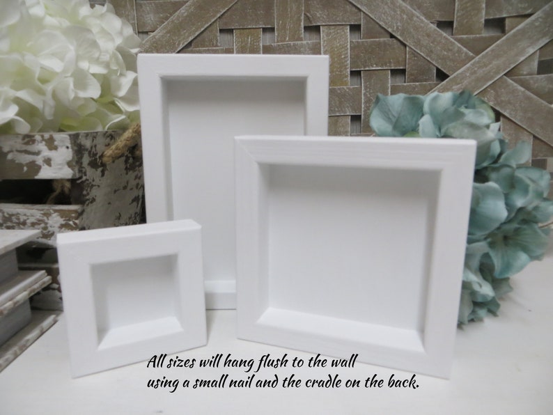 May include: Three white square picture frames of different sizes. The frames are made of wood and have a simple, modern design. All sizes will hang flush to the wall using a small nail and the cradle on the back.