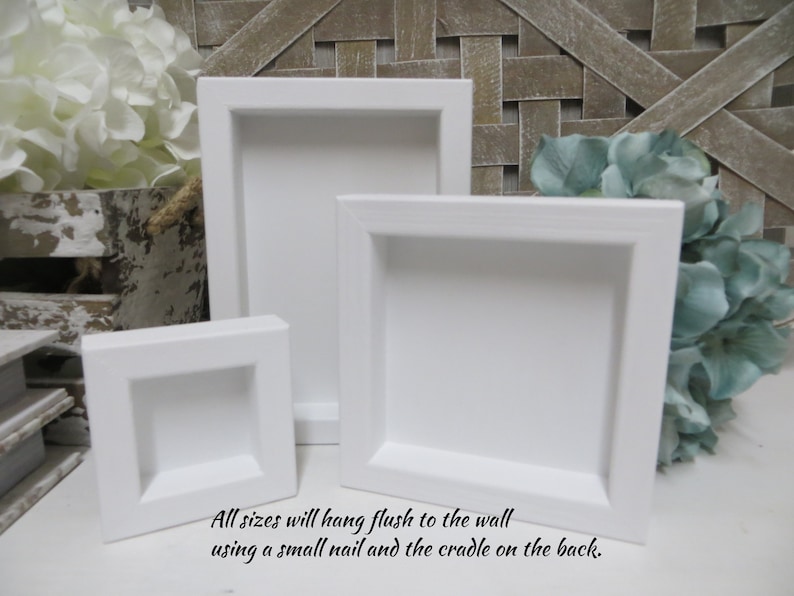 May include: Three white square picture frames of different sizes. The frames are made of wood and have a simple, modern design. All sizes will hang flush to the wall using a small nail and the cradle on the back.