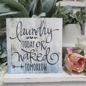 May include: A white wooden sign with a blue wash and black lettering that reads "Laundry Today Or Naked Tomorrow".