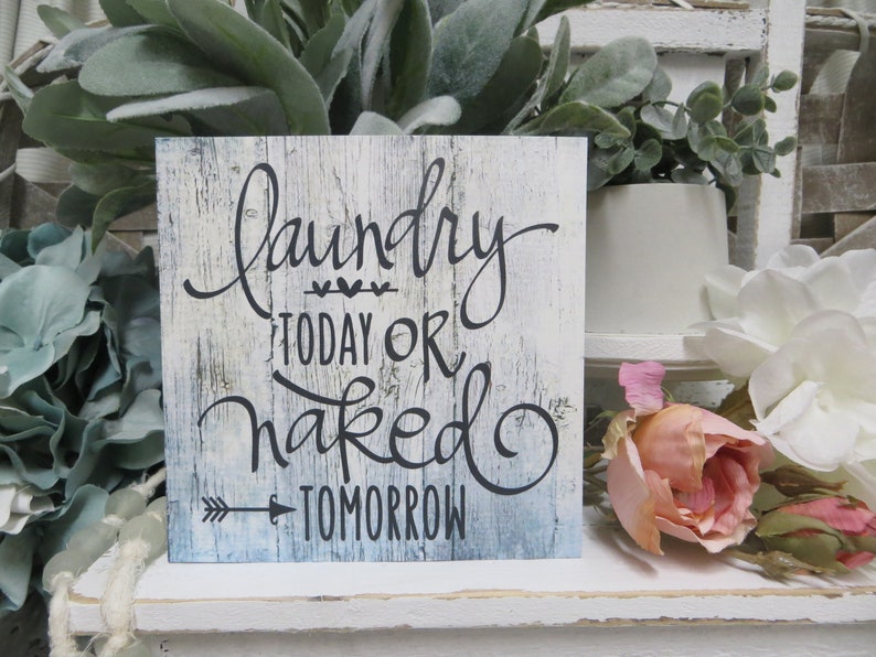 May include: A white wooden sign with a blue wash and black lettering that reads "Laundry Today Or Naked Tomorrow".