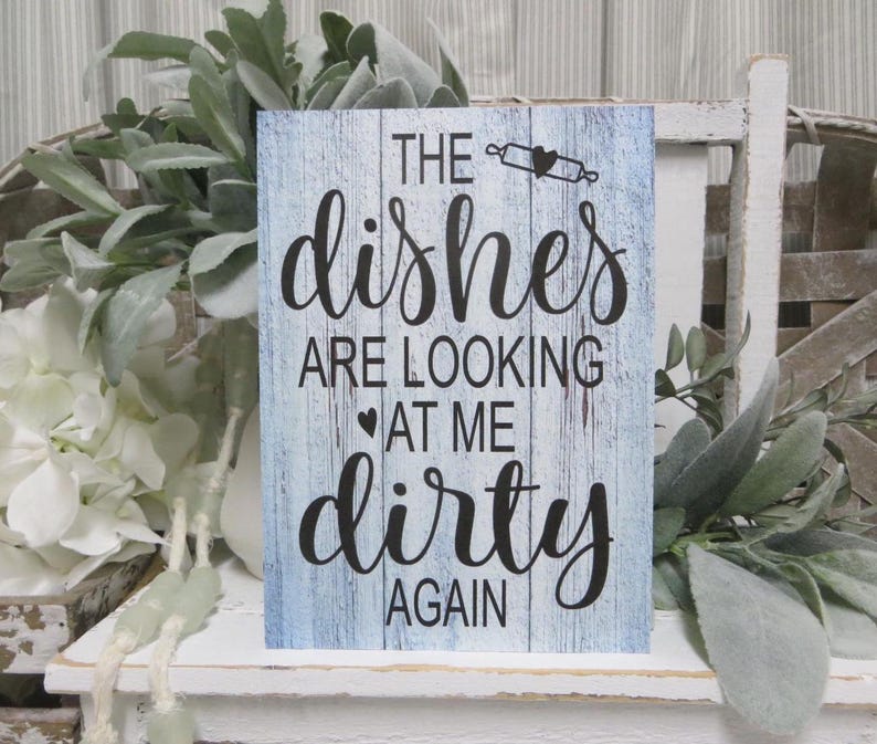 May include: A blue wooden sign with white distressed paint and black lettering that reads "The dishes are looking at me dirty again".