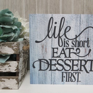 May include: A blue and white wooden sign with the text "life is short EAT dessert first." The sign has a rustic, distressed look.