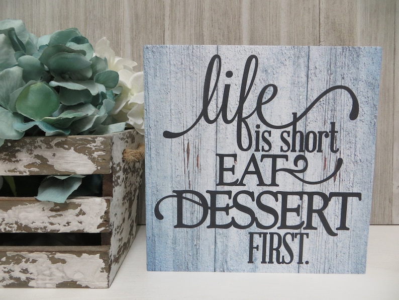 May include: A blue and white wooden sign with the text "life is short EAT dessert first." The sign has a rustic, distressed look.