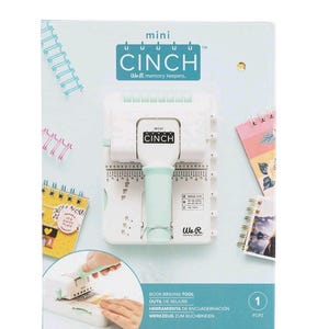 May include: A white and mint green Mini Cinch book binding tool by We R Memory Keepers. The tool is on a white background with a light blue box that has the words "mini CINCH" on it. The box also has images of notebooks and binding coils.