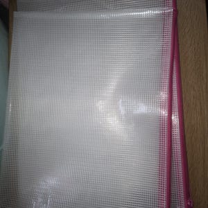 May include: Clear, grid-patterned plastic document pouches with pink zippers. The pouches are stacked, showing the texture of the material. The zippers run along the side of the pouches, providing a secure closure for the contents.