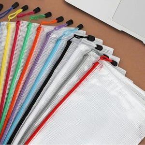 May include: A collection of clear, mesh zipper pouches in various colors, including pink, blue, yellow, green, orange, purple, black, and red. Each pouch has a matching colored zipper and a black pull tab. The pouches are arranged in a fan shape.