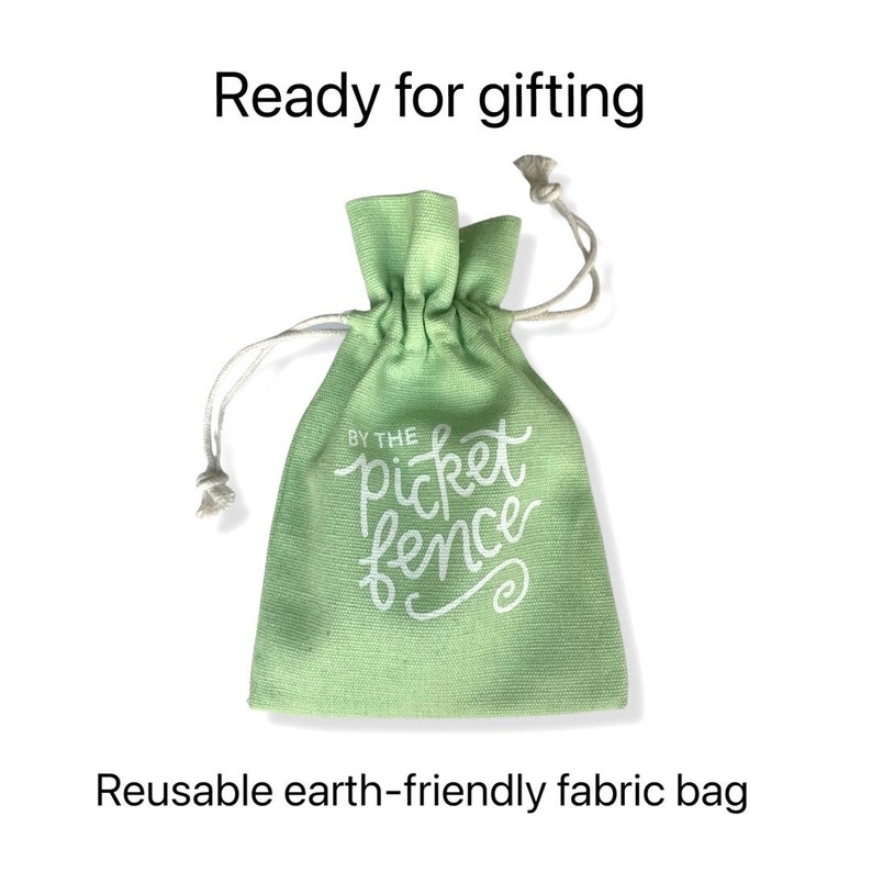May include: A light green reusable fabric bag with a white drawstring. The bag has the text "By the picket fence" printed on it.